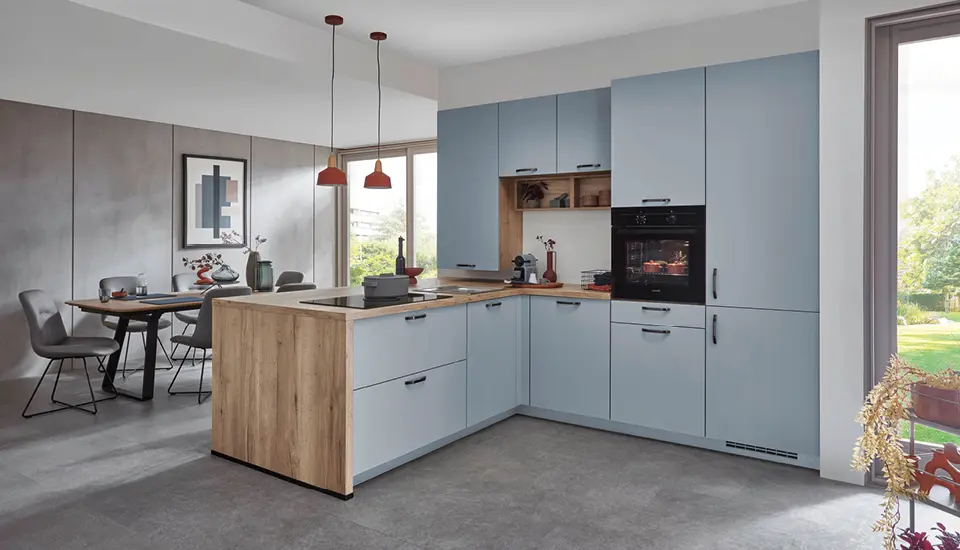 Stilvolle L-Küche in Hellblau mit Holzarbeitsplatte, Kochinsel und angrenzendem Essplatz in offenem Raum, ideal für modernes Wohnen mit harmonischem Farbkonzept.